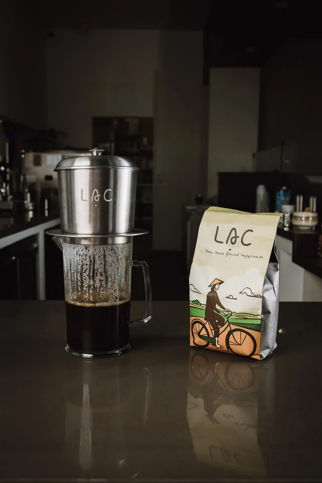 Phin filter dripping Vietnamese coffee over a bag of dark-roast beans